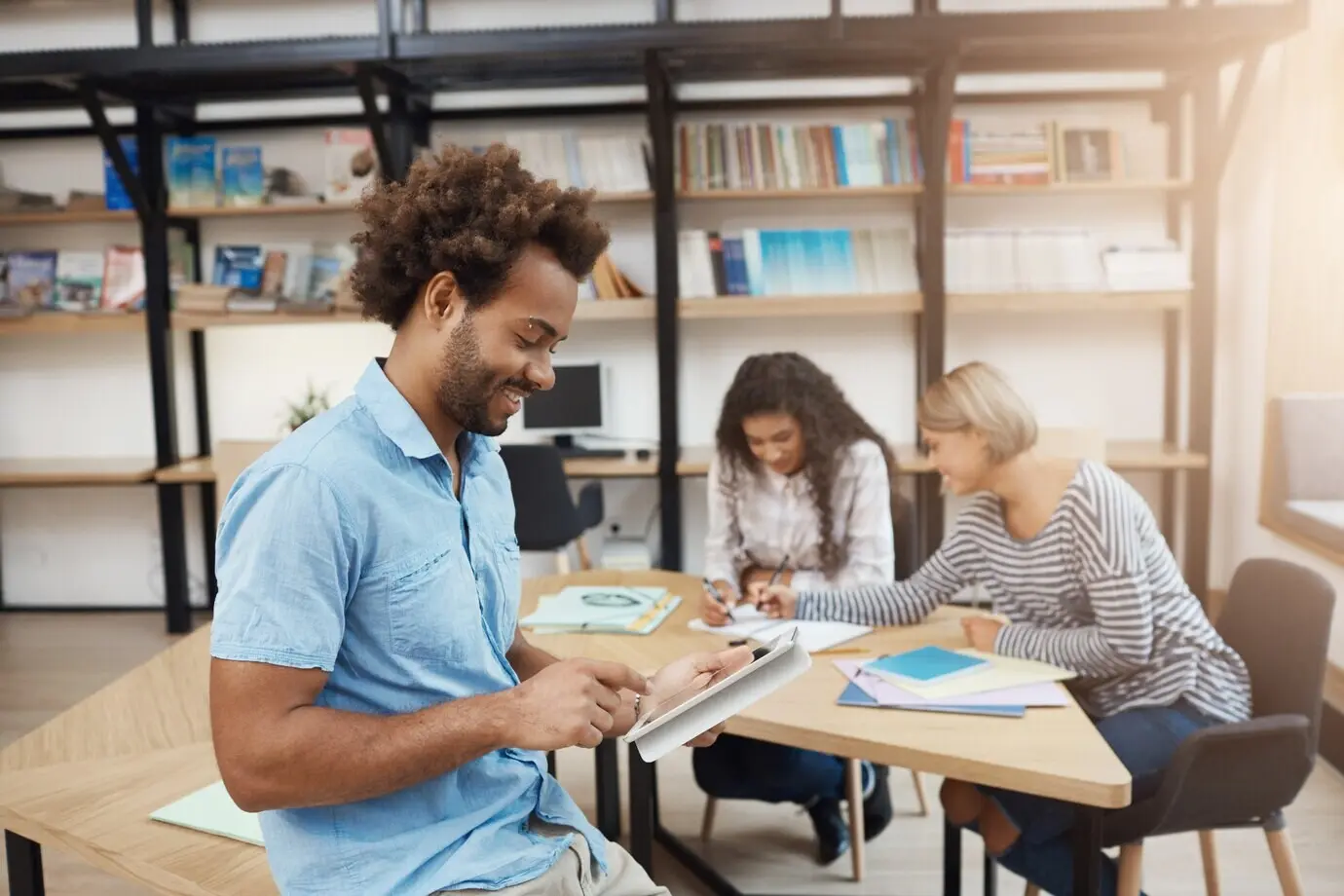 Nahaufnahme eines gutaussehenden, jungen, dunkelhäutigen angehenden Unternehmers, der auf einem digitalen Tablet nach Informationen über ein Teamprojekt sucht. Freund bei einem Meeting in der Bibliothek.
